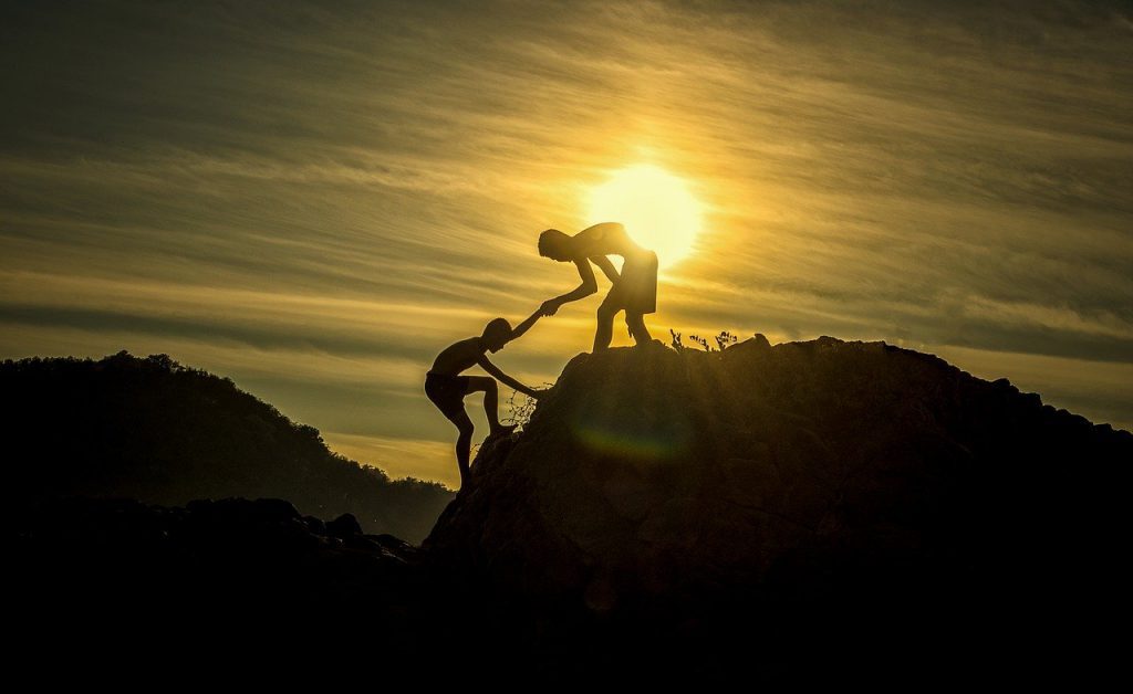 Man helping another man climb a mountain